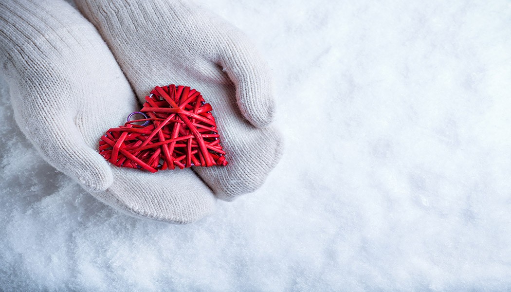 Female hands in white knitted mittens with a entwined vintage romantic red heart on a snow background. Love and St. Valentine concept.