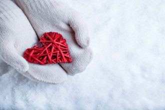 Female hands in white knitted mittens with a entwined vintage romantic red heart on a snow background. Love and St. Valentine concept.